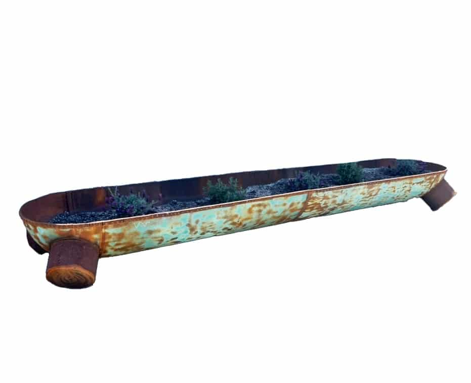 Long oval rusted steel trough planter with teal-green patina, planted with lavender, resting on rounded footed ends