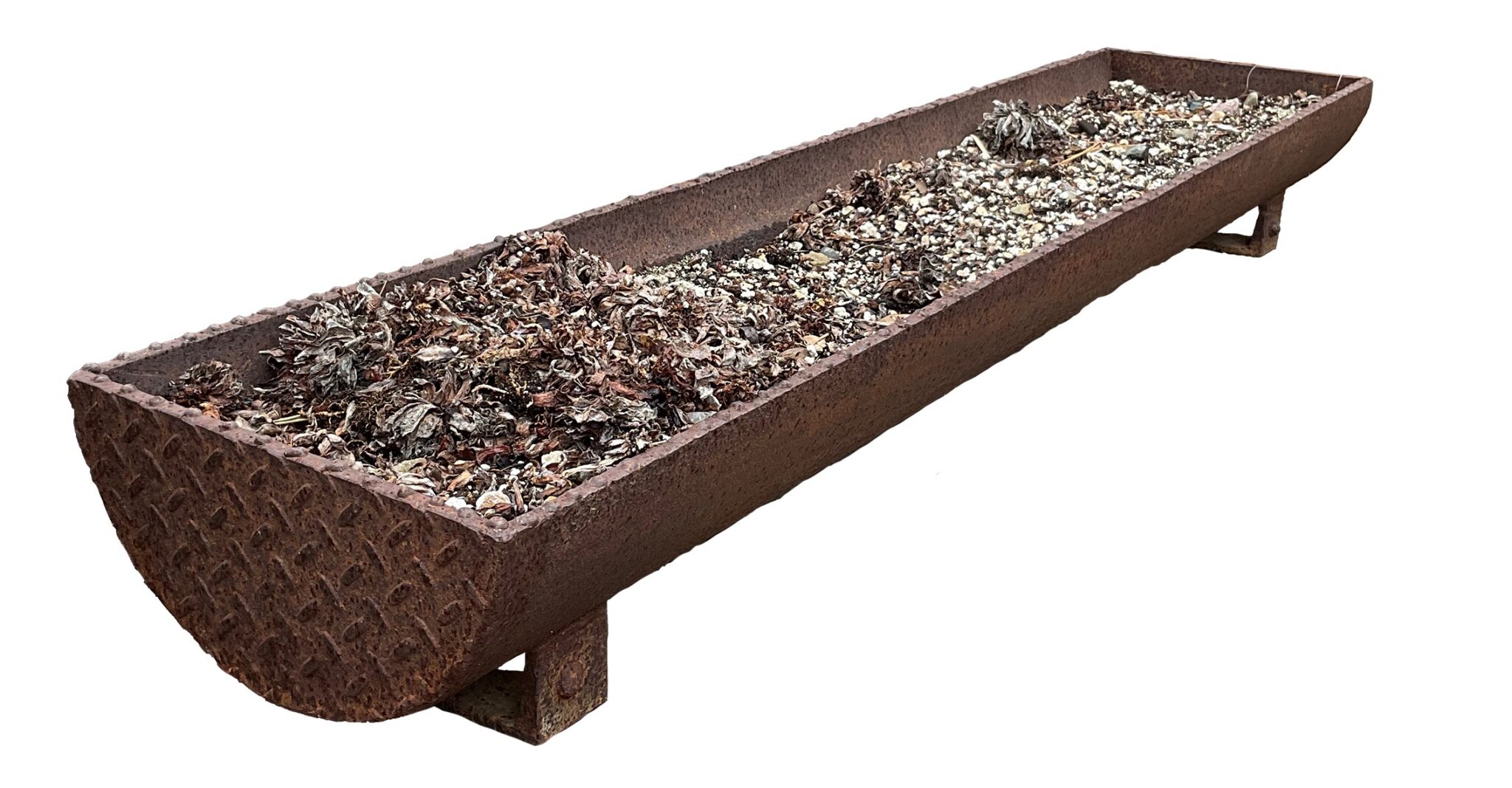 Long curved rusted steel trough planter with a textured diamond-plate end and short block feet, filled with dried foliage and stones