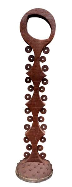 Tall rusted steel totem sculpture with an oval keyhole-shaped top, a beaded spine of small discs, and a studded round base