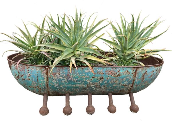 Long oval rusted steel trough planter with a riveted rim and five rounded ball-tipped feet, planted with aloe