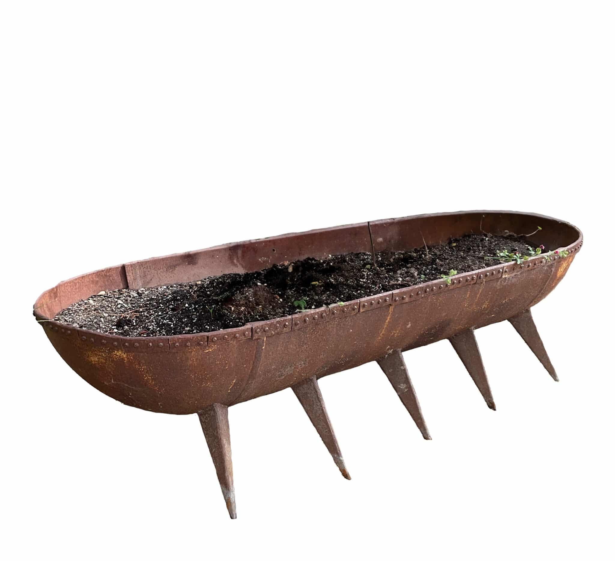 Long oval rusted steel trough planter with riveted rim, ten pointed peg feet filled with soil